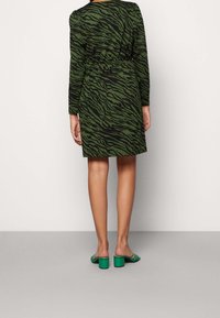 Vihreä ja musta raidallinen mekko, jossa on pitkät hihat ja elastinen vyötärö, yhdistettynä vihreisiin lohkare-korkokenkiin. Minimalistinen muotoilu.