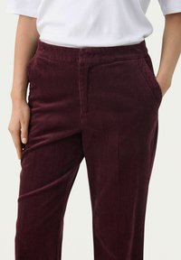 Bordeauxkleurige corduroy broek met verticale strepen, voorzien van een middelhoge tailleband en zijzakken. Zachte textuur met een ontspannen pasvorm.