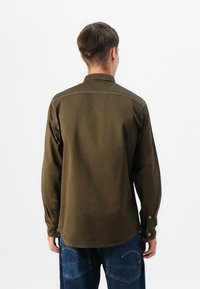 Camisa de manga larga verde oliva con cuello estándar, con cierres de botón en los puños y un dobladillo recto, fabricada en tela suave.