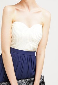 Sukienka bez ramiączek z plisowanym białym gorsetem i granatową spódnicą. Teksturalna czarna kopertówka dodaje kontrastu do stroju.