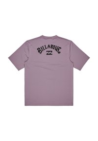 Camiseta de manga corta en tejido morado claro. Presenta el texto y el logo negro de "BILLA BONG" en la parte posterior. Textura suave, diseño sencillo.