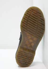 Talpa neagră de pantof, din cauciuc texturat, cu un model de profil și detalii embossate care includ un logo și instrucțiuni de întreținere.