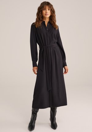 Rochie neagră, cu mâneci lungi, cu închidere cu nasturi în față, talie evidențiată cu un brâu și textură moale. Model purtând cizme negre până la genunchi.