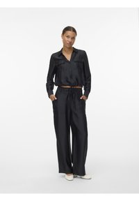 Schwarzes zweiteiliges Satin-Outfit mit einem kurzen Hemd mit Knöpfen und Taschen sowie weit geschnittenen Hosen mit elastischem Bund.