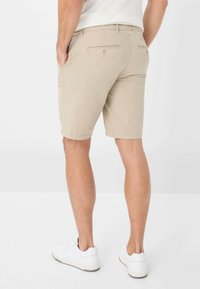 Pantaloni corti in cotone beige con una vestibilità slim, tasche posteriori e una texture liscia, abbinati a sneaker bianche.