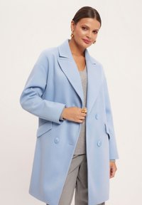 Jasnoniebieski płaszcz dwurzędowy z wyłogami, dwiema przednimi kieszeniami i okrągłymi guzikami. Miękka tekstura, luźny krój.
