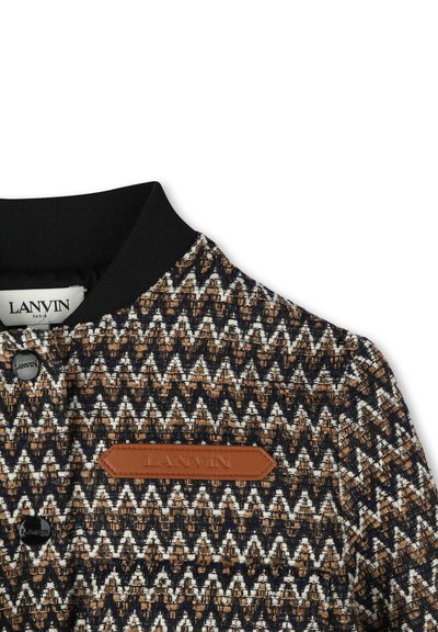 Woven jacket featuring a zigzag pattern in brown, black, and white, with a black ribbed collar and a brown leather logo patch.