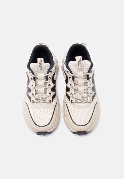 Ζευγάρι μπεζ και μαύρων αθλητικών παπουτσιών από δίχτυ με κορδόνια, παχιά σόλα και λωρίδες έλξης με την επιγραφή "WEEKEND", σε άποψη από πάνω σε λευκό φόντο.