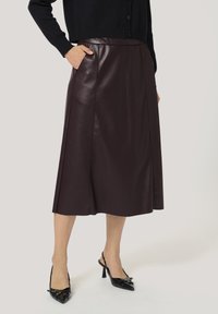 Burgundska usnjena midi krila s stranskimi žepi, gladka tekstura in sproščen silhuet, v kombinaciji s črnimi slingback petami.