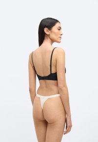 Czarny biustonosz z regulowanymi ramiączkami, wykonany z gładkiej tkaniny, z zapięciem na haczyk. W komplecie beżowe stringi z minimalnymi paskami.