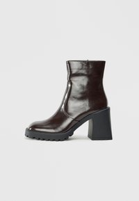 Braune Leder-Stiefelette mit glänzender Oberfläche, Blockabsatz und strukturiertem, rutschfestem Sohlenprofil. Das schlanke Design unterstreicht die moderne Silhouette.