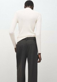 Suéter crema acanalado con cuello alto y mangas ajustadas, combinado con pantalones a cuadros gris oscuro que cuentan con bolsillos traseros y un corte entallado.