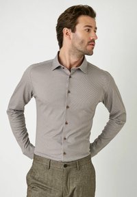 Lichtbruine overhemd met patroon, button-down kraag, lange mouwen en bruine knopen, gecombineerd met grijze op maat gemaakte broeken.