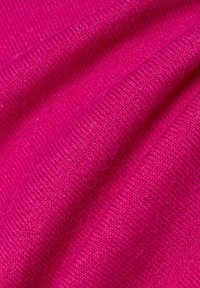 Helles pinkes Strickstoff mit sichtbarer Rippstruktur und weichen Falten.