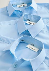 Himmelblaue Hemden von Clarks mit Knöpfen und einem glatten Stoff sowie einem sauberen Stich entlang des Kragenrandes und der Knopfleiste.