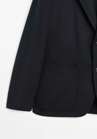 Manche et partie avant d’un manteau en laine noire avec grande poche plaquée et fermeture partielle par boutons sur fond blanc.