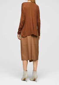 Pull marron surdimensionné à manches longues, associé à une jupe midi en cuir beige et des bottines gris clair à bout pointu et fermeture éclair.
