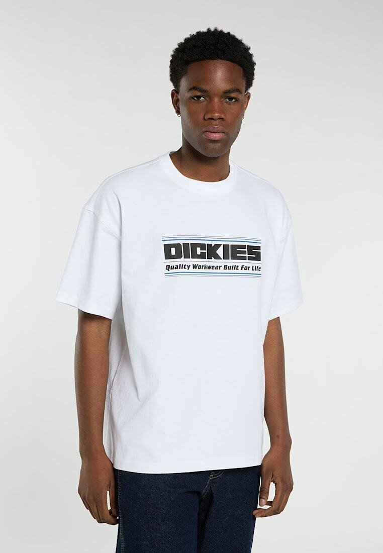 Young man stands wearing a white Dickies T-shirt with black text "Quality Workwear Built For Life" and dark blue jeans against a plain background.