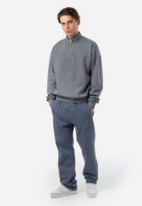 Grå half-zip sweatshirt med lange ermer, kombinert med lyseblå joggebukser. Begge laget av myk tekstil, med avslappet passform og lommer.