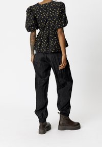 Blusa nera con motivo floreale, maniche a sbuffo e vita cintrata, abbinata a pantaloni neri testurizzati e stivali alla caviglia marroni.