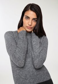 Maglione grigio a maglia con maniche lunghe e bordo a coste. Texture morbida, scollo a girocollo e sottili variazioni nel filato.