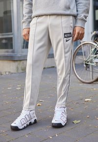 Ljusgrå Nike-träningsbyxor med svarta sidsränder och logotyp. Bärs med vita sneakers med framträdande "AIR"-bokstäver och röda detaljer.