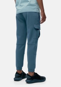 Pantaloni cargo blu con vita e polsini elasticizzati, dotati di tasche laterali; abbinati a scarpe da atletica nere con dettagli testurizzati.