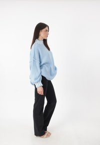 Lichtblauwe oversized trui met een hoge hals en textuurstof; voorzien van witte en blauwe gestreepte manchetten. Geverfd met zwarte broek.