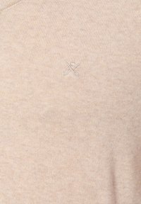 Beige gebreid sweater met een zachte textuur, voorzien van een klein geborduurd scharenlogo boven de linker borst. Rond decolleté ontwerp.