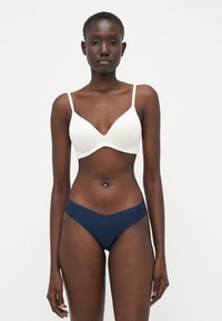 Witte bralette met een diepe halslijn en dunne bandjes, gecombineerd met marineblauwe hooggerokte slipjes met een V-vormige snit. Zachte textuur.