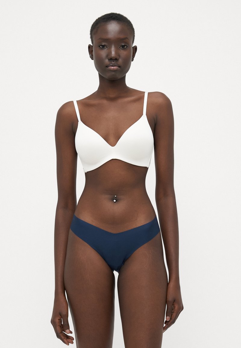 Witte bralette met een diepe halslijn en dunne bandjes, gecombineerd met marineblauwe hooggerokte slipjes met een V-vormige snit. Zachte textuur.