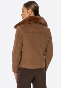 Braune Wildlederjacke mit einem großen Kragen aus Kunstfell, Reißverschluss und tailliertem Schnitt. Zu den Merkmalen gehören eine Nahtdetail und eine kurze Länge.