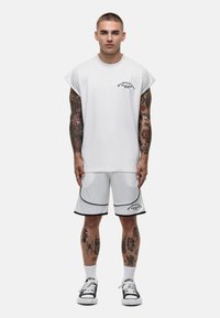 Witte oversized T-shirt met ronde hals en korte mouwen, gecombineerd met witte shorts met zwarte accenten. Beide hebben grafische tekstdetails.