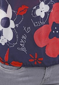 Marinfärgad tyg med röda och vita blommönster samt läpptryck. Texten säger "lär dig att kyssa." Har en böjd nederkant och sömdetaljer.