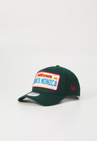 Căciulă de baseball verde cu margine plată, având un patch brodat colorat care scrie "California 1990 SANTA MONICA" și accente roșii.