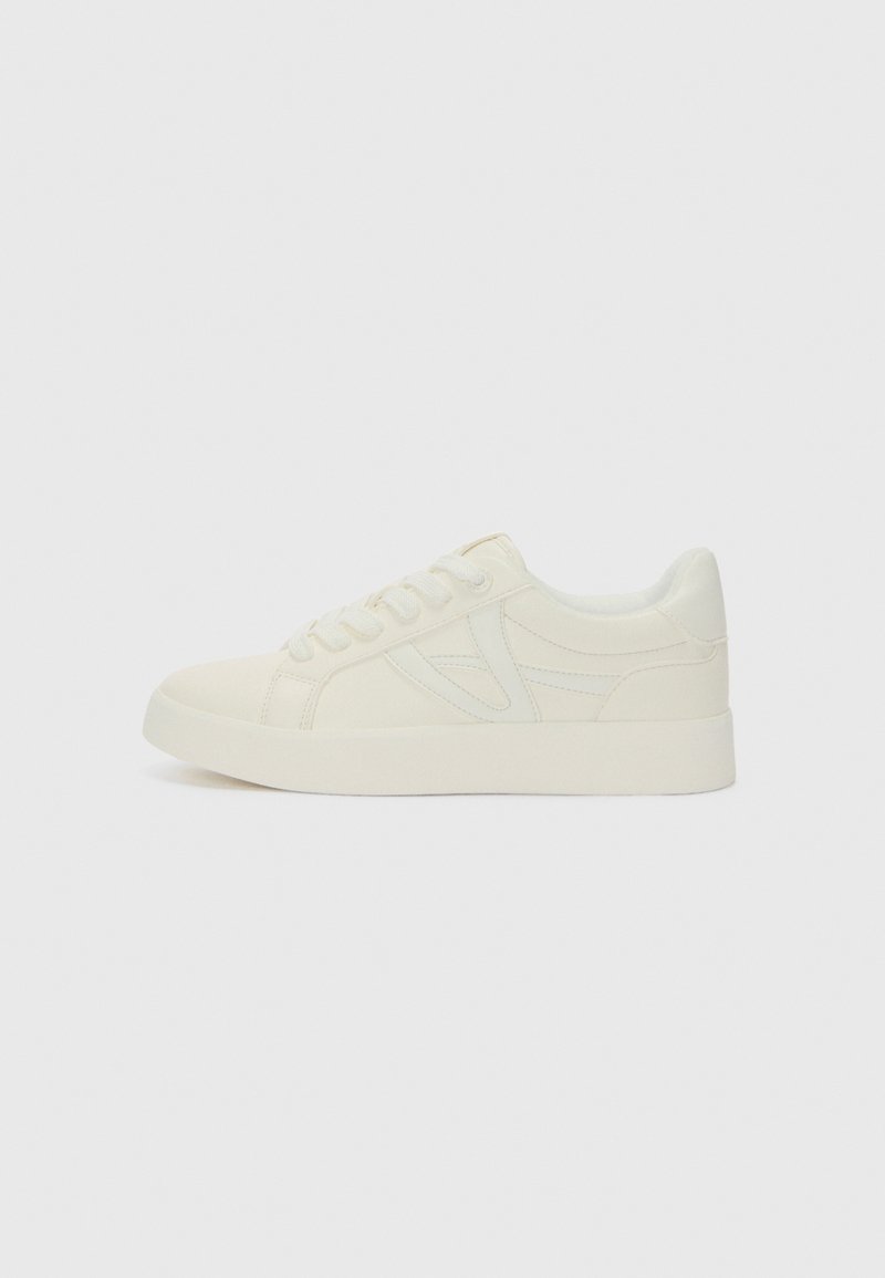 Sneakers bianchi in tela con design a profilo basso, caratterizzati da una superficie testurizzata, punta rotonda e lacci coordinati. Dettagli laterali sottili.