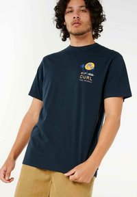 Navy blue cotton t-shirt featuring a yellow and blue palm tree graphic with text "RIP CURL THE SEARCH" on the left chest. Short sleeves.