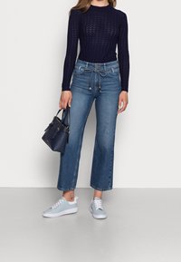 Navy knitted long-sleeve top, high-waisted wide-leg blue jeans, light blue sneakers, and a small navy handbag with gold accents.