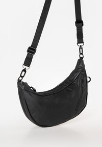 Schwarze Umhängetasche mit kurvenförmigem Design, aus glattem Material gefertigt. Verfügt über einen verstellbaren Tragegurt, eine Reißverschlusstasche und metallische Hardware-Details.