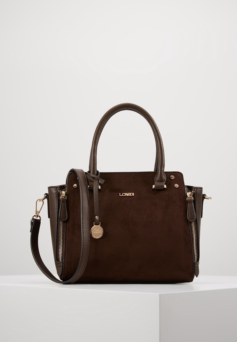Sac à main en cuir marron foncé avec double poignée, bandoulière amovible, logo de la marque à l'avant, poches latérales zippées et un charm rond doré.