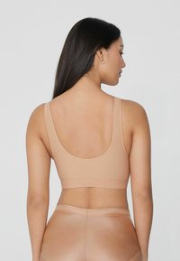 Nahá bezešvá sportovní podprsenka se širokými ramínky a kulatým zadním dílem. Materiál je hladký a elastický, navržený pro pohodlí a podporu.