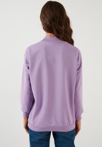 Felpa viola con collo e polsini a costine, caratterizzata da una texture liscia e una vestibilità morbida, mostrata da dietro.