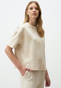 Crème short-sleeve top met bloemenborduursel in een licht verhoogde textuur. Relaxte fit met een ronde halslijn en eenvoudige ontwerpelementen.