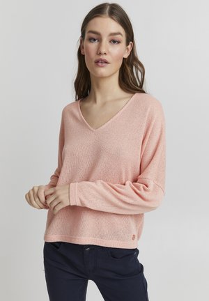Pull en tricot rose avec un col en V, des épaules tombantes et des manches longues. Le tissu a une apparence texturée et légère.