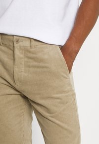 Beiga kordflorsbyxor med ribbat mönster, knappstängning, sidofickor och rak passform, delvis visade nära midjan.