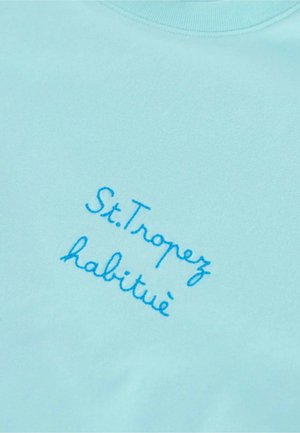 Pullover azzurro chiaro con testo ricamato; la scritta recita "St. Tropez habitué." Tessuto liscio, design con scollatura a girocollo.