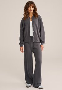 Pelēks džemperis ar pogām, brīvs piegriezums un ribotām piedurknēm, apvienots ar atbilstošiem pelēkiem plašiem biksēm. Gluda auduma, ikdienas dizains.