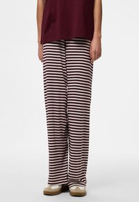 Stripede pyjamasbukser i burgunder og creme, lavet af ribstrikket stof. De har en løs pasform og et lige ben-design med en blød tekstur.