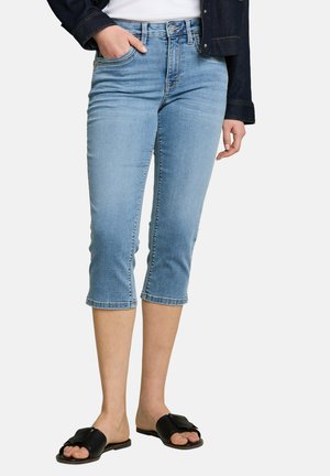 Lichtblauwe cropped skinny jeans gedragen met zwarte open teen slip-on sandalen en een donkeren spijkerjas.