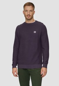 Paarse gebreide sweatshirt met een ronde hals en ribbels bij de mouwen, voorzien van een klein logo-oprafk op de borst. Gecombineerd met groene broeken.